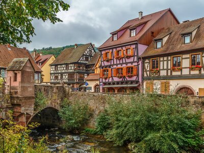 Colourful tradtitonal houses in Kaysersberg with old stone bridge and slow moving water beneath, Alsace, France