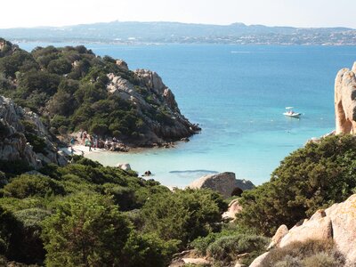 Coastal view in Sardinia with small group of walkers enjoying small sandy beach near water, Italy